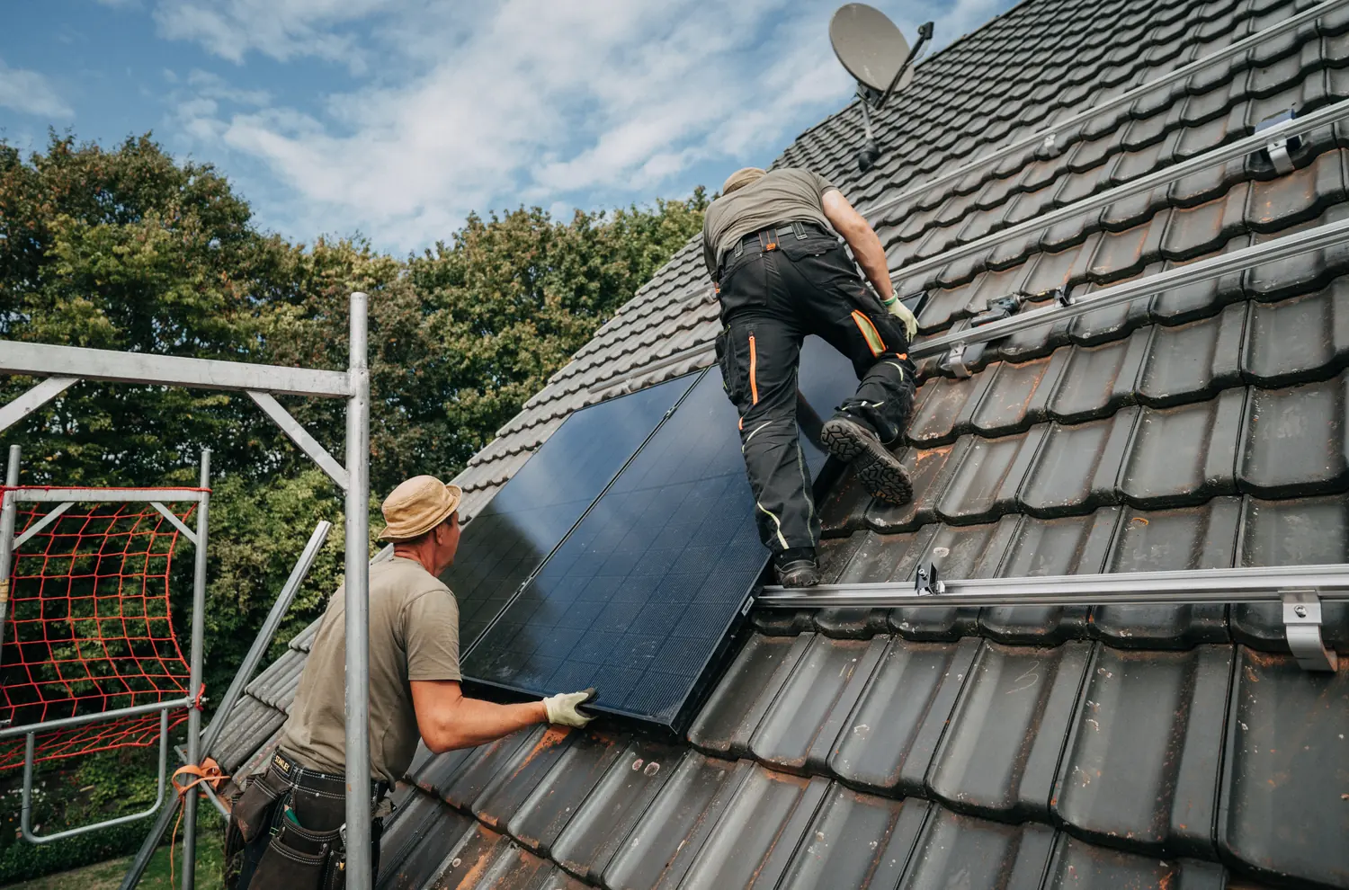 Zwei Monteure von Heye-Enneking setzen ein Solarmodul auf einem Ziegeldach ein