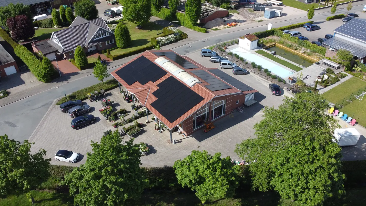 Volldachbelegung mit schwarzen Modulen auf dem Ziegeldach eines Gartencenters, Luftaufnahme