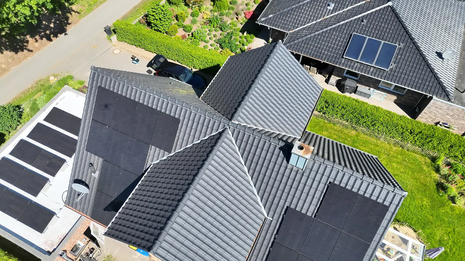 Module auf mehreren Dachflächen eines Wohnhauses mit dunklen Ziegeln, Luftaufnahme