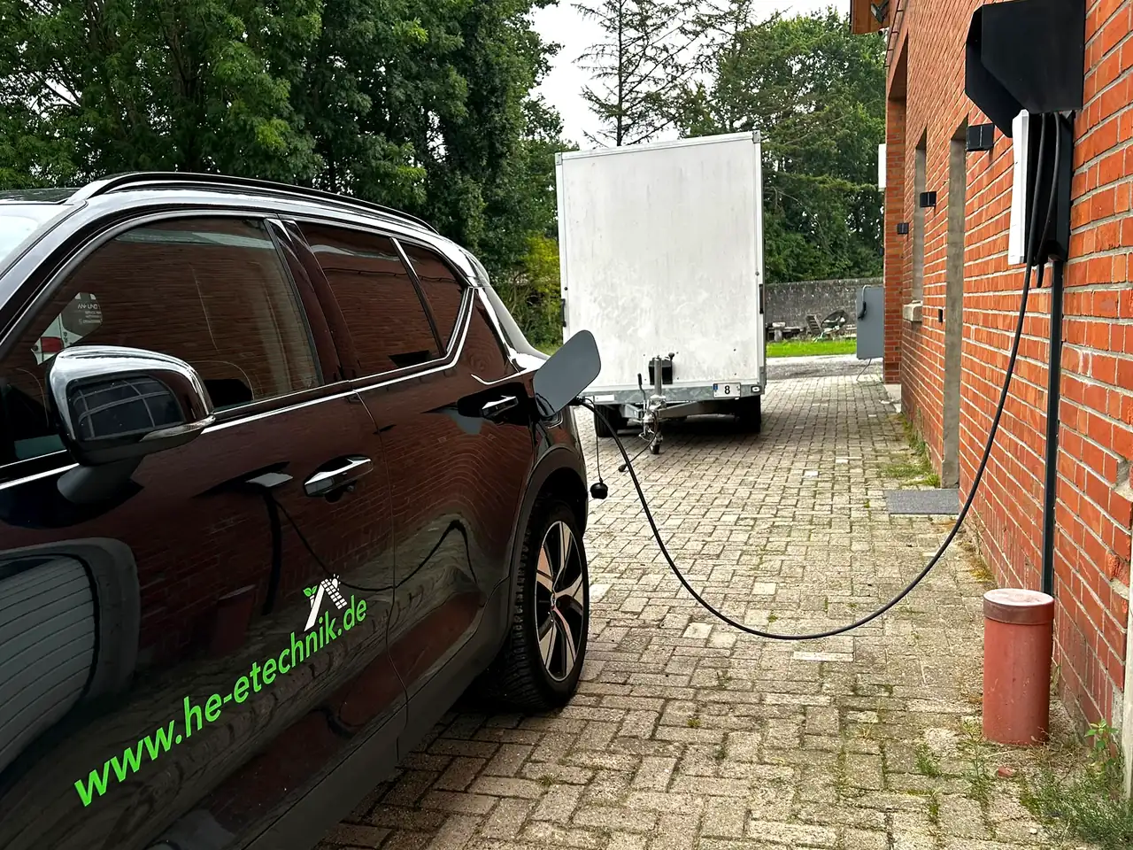 Volvo XC40 mit Firmenbeschriftung lädt an einer von Heye-Enneking installierten Wallbox an der Klinkerwand